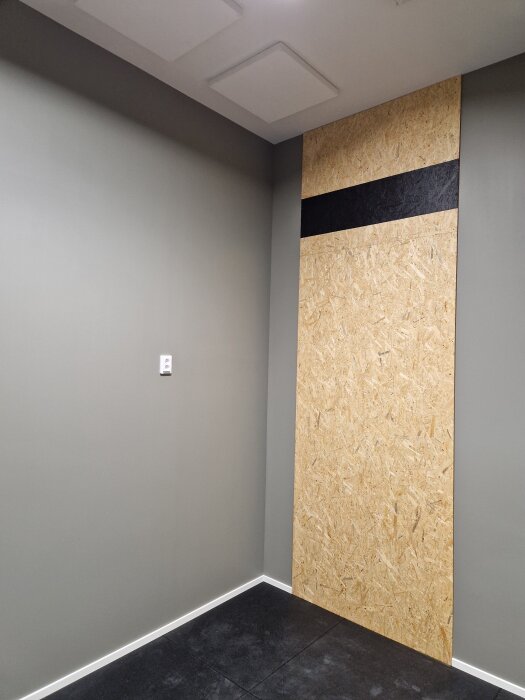 Gråmålat rum med grått tak och mörk klinker. En väggpanel i trä med en svart rand är installerad för att skapa ett gym.