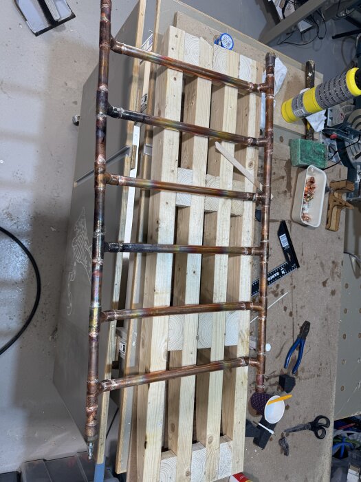 Handdukstork i koppar under uppbyggnad med synliga skarvar och verktyg, inklusive MAP-gasbrännare, på arbetsbänk med träunderlag.