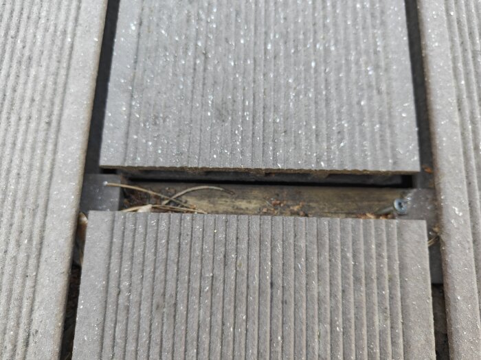 Närbild av altangolv i komposittrall med synliga springor mellan brädorna, där smuts och skräp har samlats.