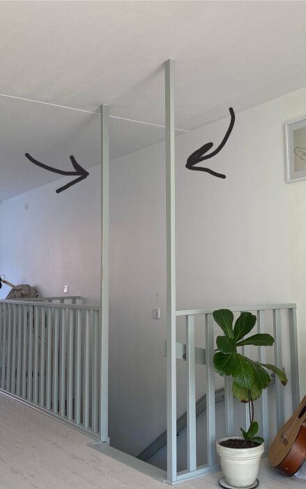 Trappa med två lodräta pelare som går från golv till tak vid räcket, pilar pekar på dem. Brevid står en krukväxt vid trappans öppning.