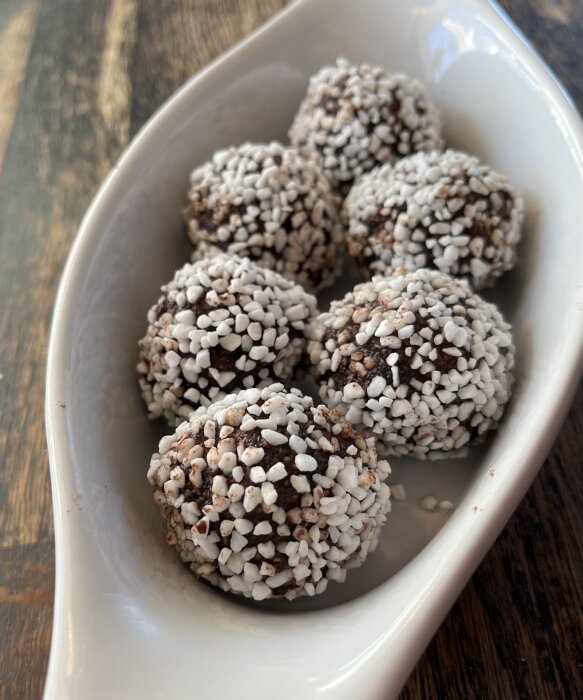 Skål med sex chokladbollar rullade i pärlsocker, på ett mörkt träbord.
