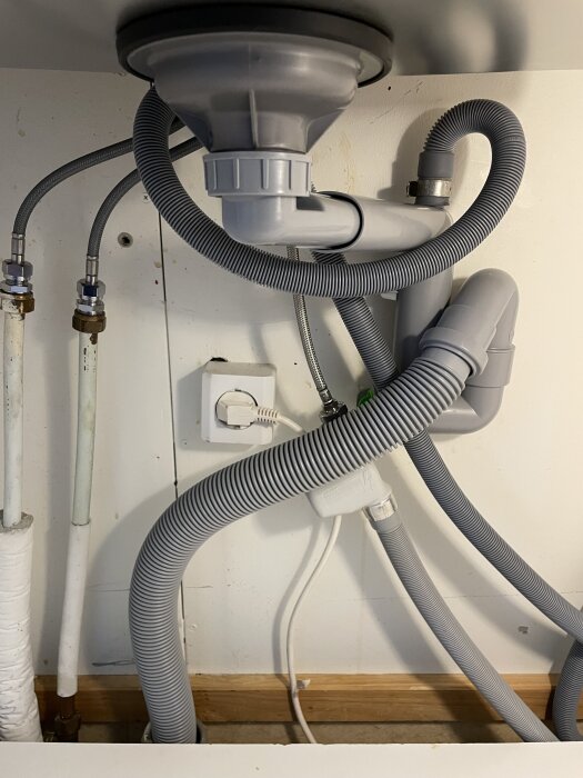 Under diskbänken med synliga röranslutningar och en grå avloppsslang kopplad till tvättställ.