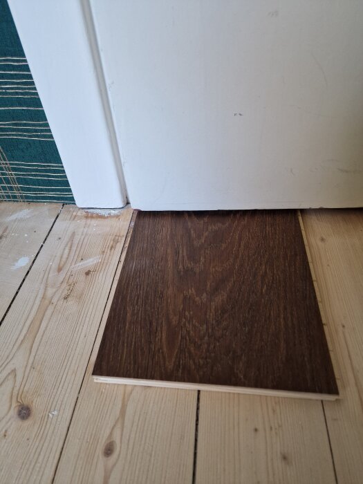 Nära bild av en omålade trägolv och en parkettbräda placerad vid en dörrtröskel, med tanke på en golvrenovering.