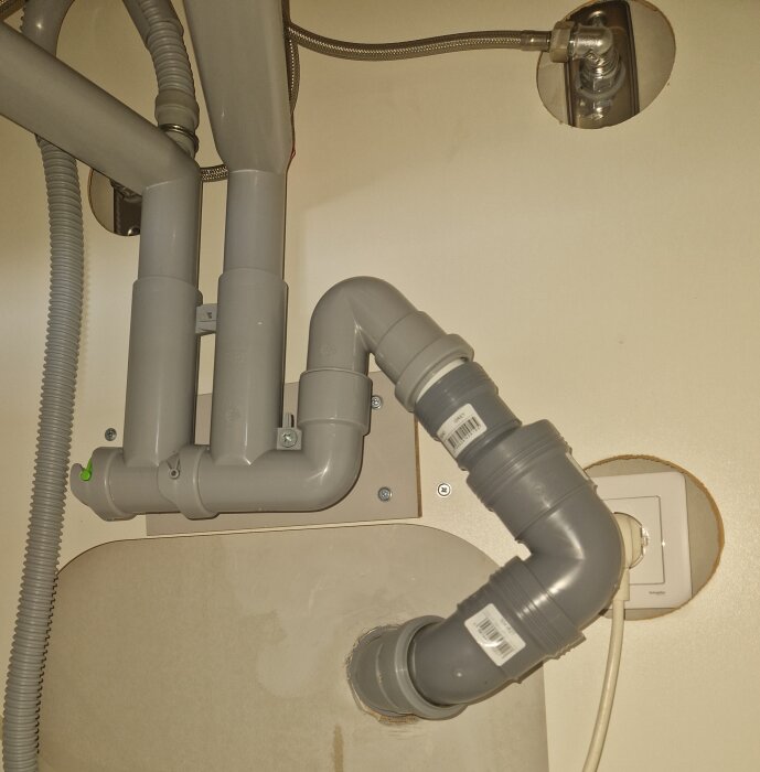 Rörinstallation under diskho, grå plaströr kopplade med böjar och anslutna till vattenledning.
