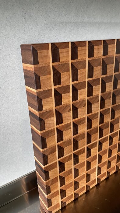 Träskärbräda med kubmönster i olika träslag, stående på en bänkskiva.