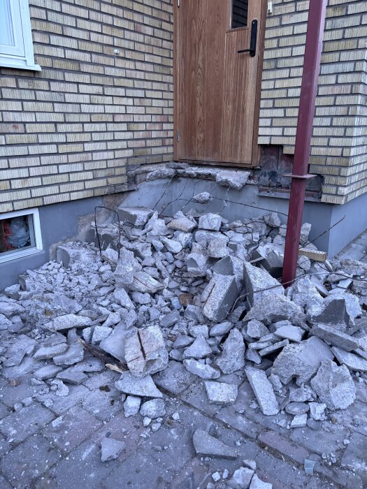 Stentrappa har rasat framför en ytterdörr, med murbruk och tegelbitar utspridda på marken.