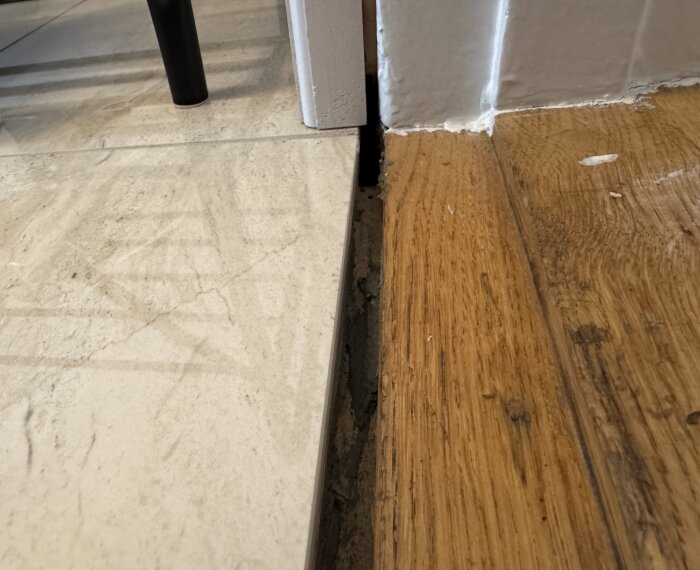 Glapp mellan granitkeramik och tröskel i entréhall. Golvlister syns inte, och träytan har ojämn färg. Utmaning med övergångsdetaljer.
