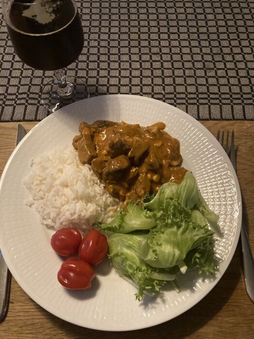 Pork Tikka Masala med ris, sallad och cocktailtomater på en tallrik, bredvid en ölglas.