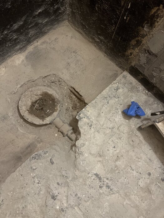Renoveringsprojekt i badrum med synligt gammalt betonggolv och avloppsrör, förberett för byten och förhöjning av golv.