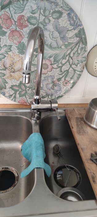 Nyinstallerad köksblandare i rostfritt med en blå trasa hängande över diskbänken, blommigt underlägg i bakgrunden.