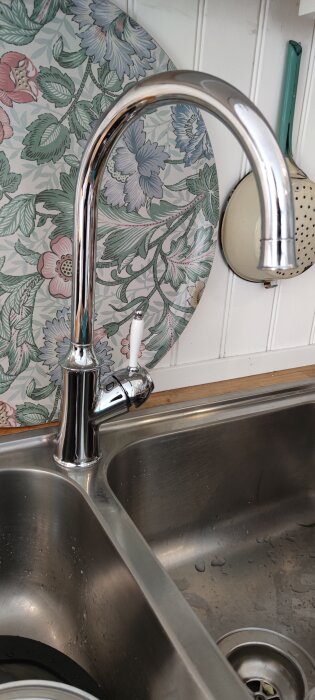 Nyinstallerad köksblandare i krom ovanför en diskbänk, mot en bakgrund med blommigt mönster.