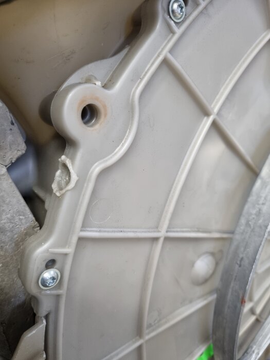 Plastlock med synliga skruvar och en smält fog på maskindel, nära en trumma, kanske en tvättmaskin, där trummans rotation diskuteras.