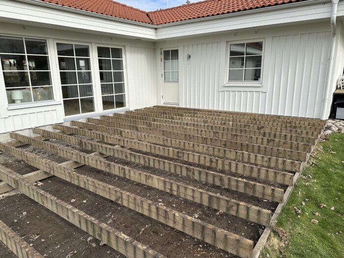 Uppbruten altan utan trall visar reglar och jord vid vit fasad, del av renoveringsprojekt från 1998.