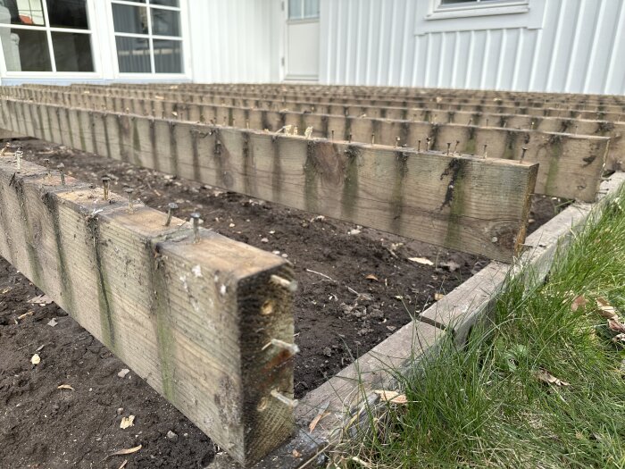 Rivna trallgolv med synliga reglar och bärlinor på en altan från 1998 under renovering, jord och gräs syns vid sidan.