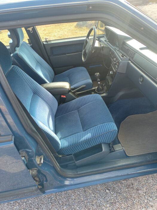 Interiör av en gammal bil med blå säten och instrumentpanel, fotograferad från passagerarsidan.