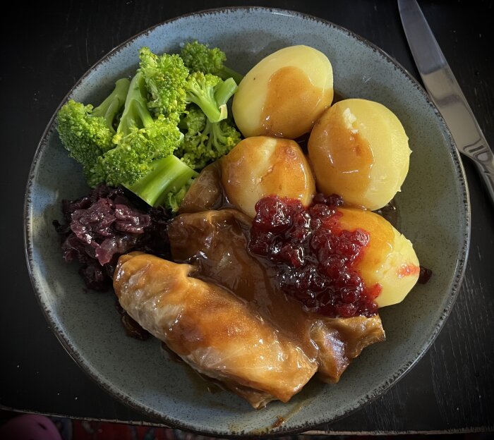 Tallrik med kåldolmar, kokt potatis med sås, broccoli, rödkål och lingonsylt.