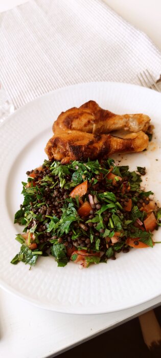 Tallrik med tabbouleh av belugalinser, persilja och tomater, serverad med grillad kyckling.
