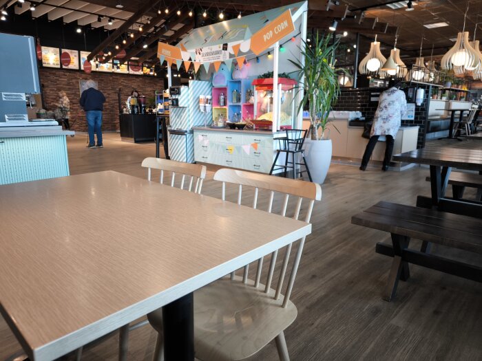 Lunchrestaurang med tomma bord, popcornmaskin och matdisk i bakgrunden samt personer som serverar sig själva.