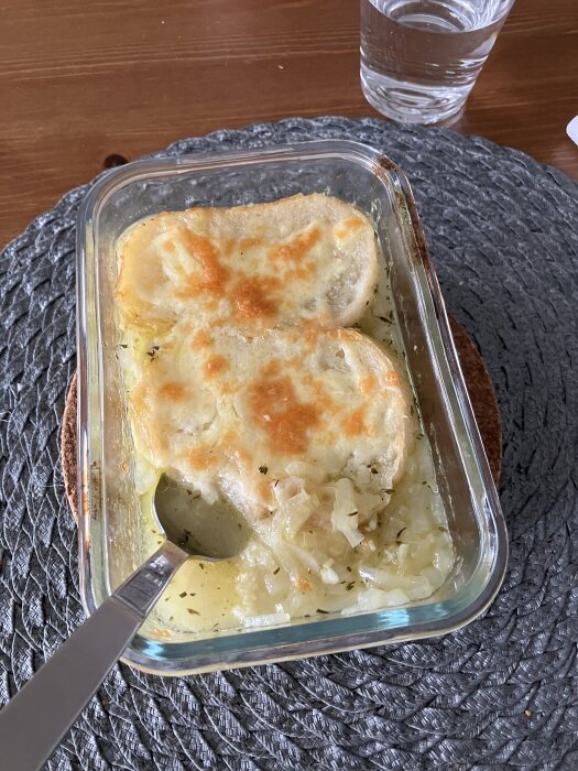 Ugnsform med fransk löksoppa toppad med ost och med knäckebröd på sidan, serverad med en sked.