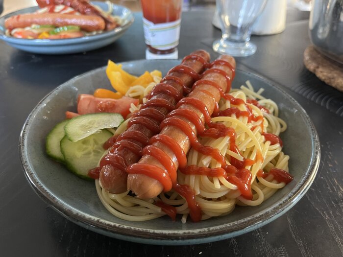 Stekt korv med hög kötthalt och spaghetti toppad med ketchup, samt grönt som gurkskivor och paprika på en tallrik.