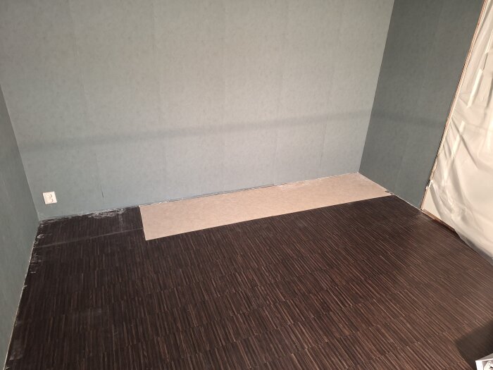 Sovrum med delvis täckt golv där en ljus matta saknas under tidigare garderober, omgiven av mörkt vinylgolv och gröna väggar.