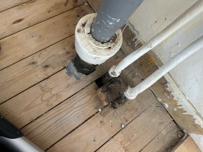 Rör och vitmålad råspont i köksrenovering, med vattenrör som behöver tätning innan golvläggning.