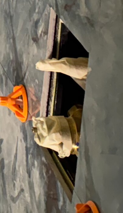 Öppen vägg med PEX-rör täckt i skyddsmaterial och orange verktyg för kakeljustering, eventuell plats för reparation av skadat rör i badrum.