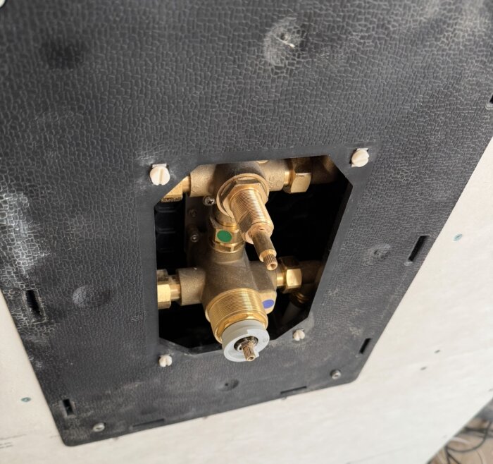 Inbyggd duschventil med synliga kopplingar och röranslutningar i ett duschutrymme under renovering, delvis bakom panel.