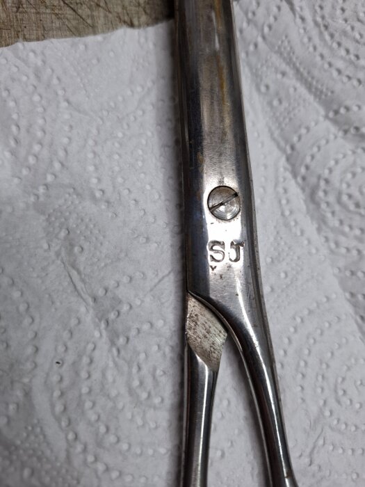 Verktyg i metall med skruv och initialerna "SJ", ligger på ett papper.