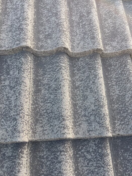 Grå takpannor av betong, del av takbeläggning. Märke Zanda, oidentifierad modell. Stora strukturerade ytor med skuggade kanter.