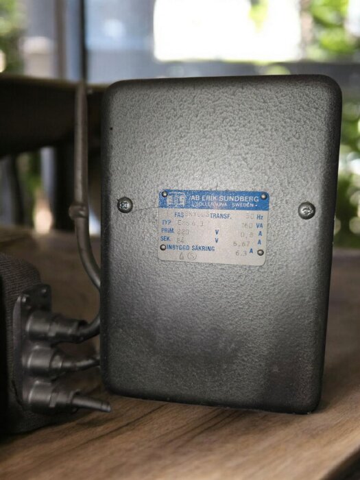 En fas-skyddstransformator från AB Erik Sundberg med etikett och anslutna kablar, stående på ett bord.