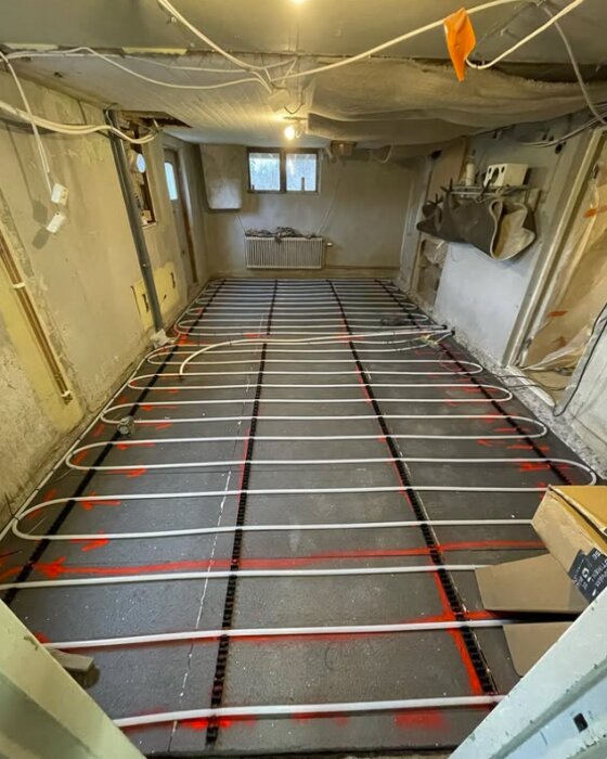 Golvvärmeinstallation i ett rum; rör lagda över isoleringsmaterial visar stegen i renoveringsprocessen för att skapa ett energieffektivt golv.