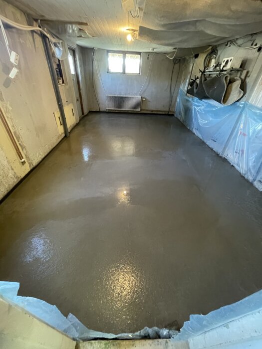 Nylagt betonggolv i ett renoveringsutrymme med genomskinlig plast längs kanterna och byggmaterial på sidan.