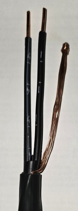 Svart och kopparfärgad EKKJ-kabel med tre ledare, varav två är isolerade i svart plast och en är koncentrisk som används för jordning.