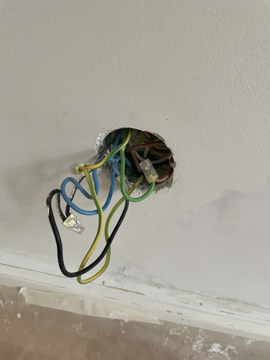 Kablar sticker ut ur ett runt hål i väggen, med klämmor på några av dem, förberett för installation av ett infällt vägguttag i ett tidigare kök.