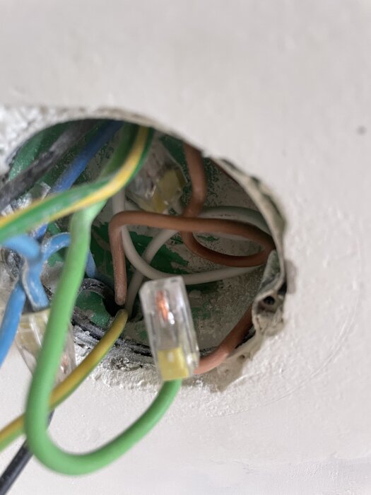 Elektriska trådar i en väggbox, med plastklämmor och synliga kablar i olika färger, i ett tidigare köksrum.