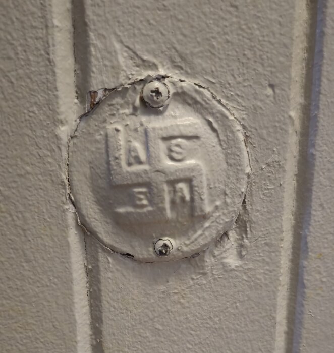 Rund metallåda med ASEA-logga på vägg, målad i samma färg som väggen. Eventuellt original från 1920-talet.