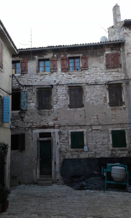 Gammalt stenhus i Rovinj med slitna fönsterluckor och en grön dörr. Huset står vid en kullerstensgata.