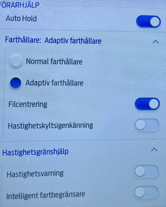 Inställningsmeny i bil, aktiv adaptiv farthållare, autohold och filcentrering på, hastighetsgränshjälp och skyltigenkänning av.