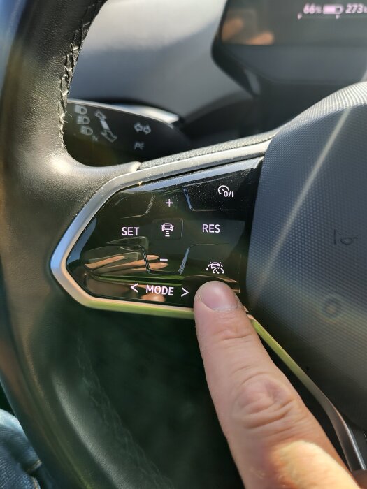 Finger trycker på MODE-knappen på en bilratt för att ändra funktion eller inställning.