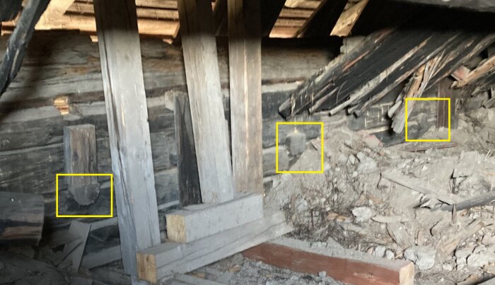 Bilden visar en lada med delvis nedfallna och avsågade träbjälkar, omgiven av bråte och skadade väggar, vilket pekar på tidigare konstruktion.