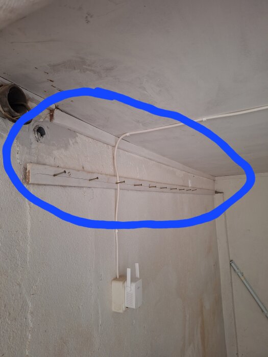 Bild på en vägg med spår efter frigolitskiva och ett överliggande kabelrör, blått område markerar hörnan i ett källarrum.