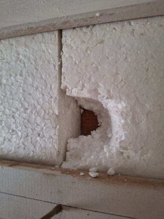 Frigolitskiva med hål i ett källarrum, visar trä på andra sidan.