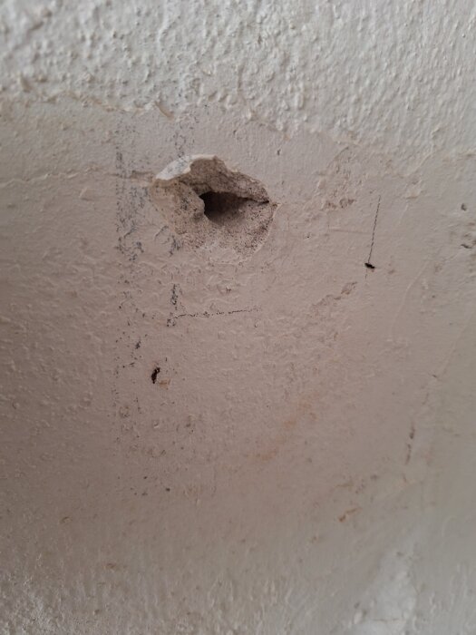 Hål i en vitmålad vägg av betong eller murverk i ett hus från 40-talet.