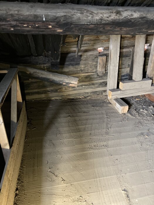 Golv i uthus med synligt mellanrum mellan golvlist och golv, visar sättning. Obehandlat trägolv och del av timmervägg syns.