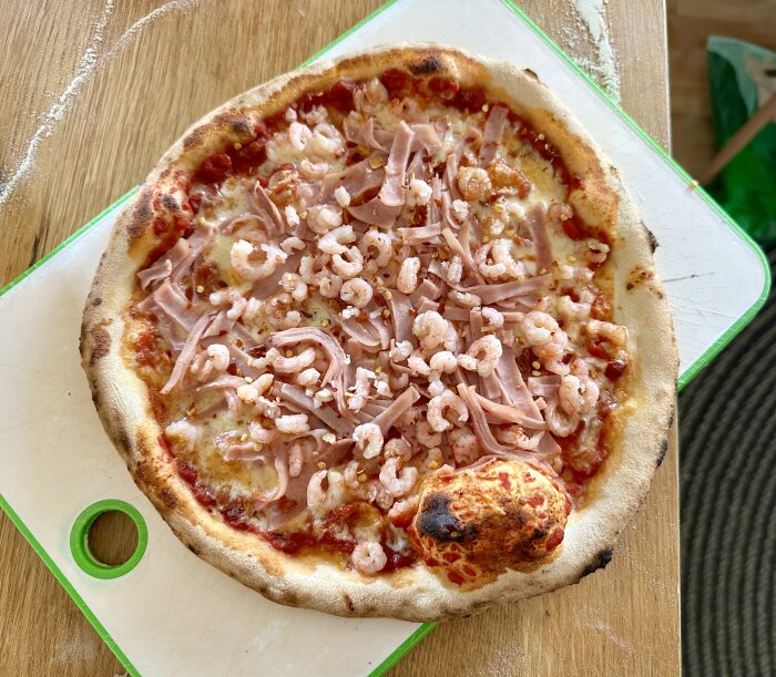 Pizza med räkor och skinka på en skärbräda av trä.