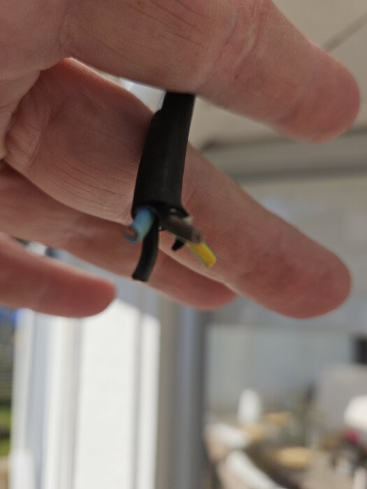 Närbild på en hand som håller fyra kablar: gul, blå, svart och brun, som ska kopplas till en Somfy markismotor.