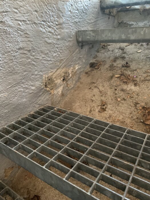 Utomhus källartrappa med lösa metallsteg och en betongvägg. Trappstegen sitter fast i betongen med plugg och skruv.