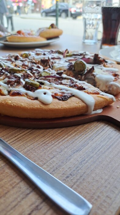 Pizza med pulled beef, BBQ-sås, jalapeños och vit sås på ett bord, med glas och tallrikar i bakgrunden.