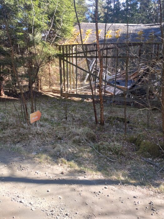 En övergiven träbyggnad på en naturtomt med en "till salu"-skylt i förgrunden.